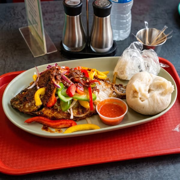 Grilled whole fish topped with colorful peppers and onions, served with fufu and sauce.