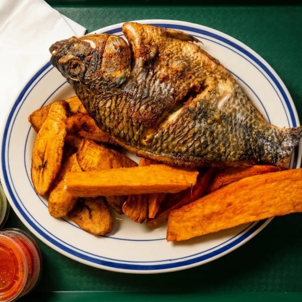 Fried whole fish with plantains and sweet potato fries on a white plate with blue stripes.