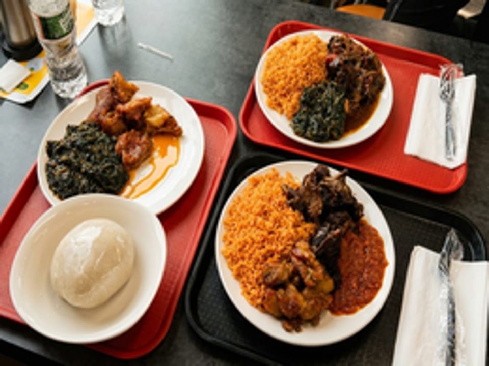 Three plates of West African food, including jollof rice, stewed meats, and fufu, on trays.