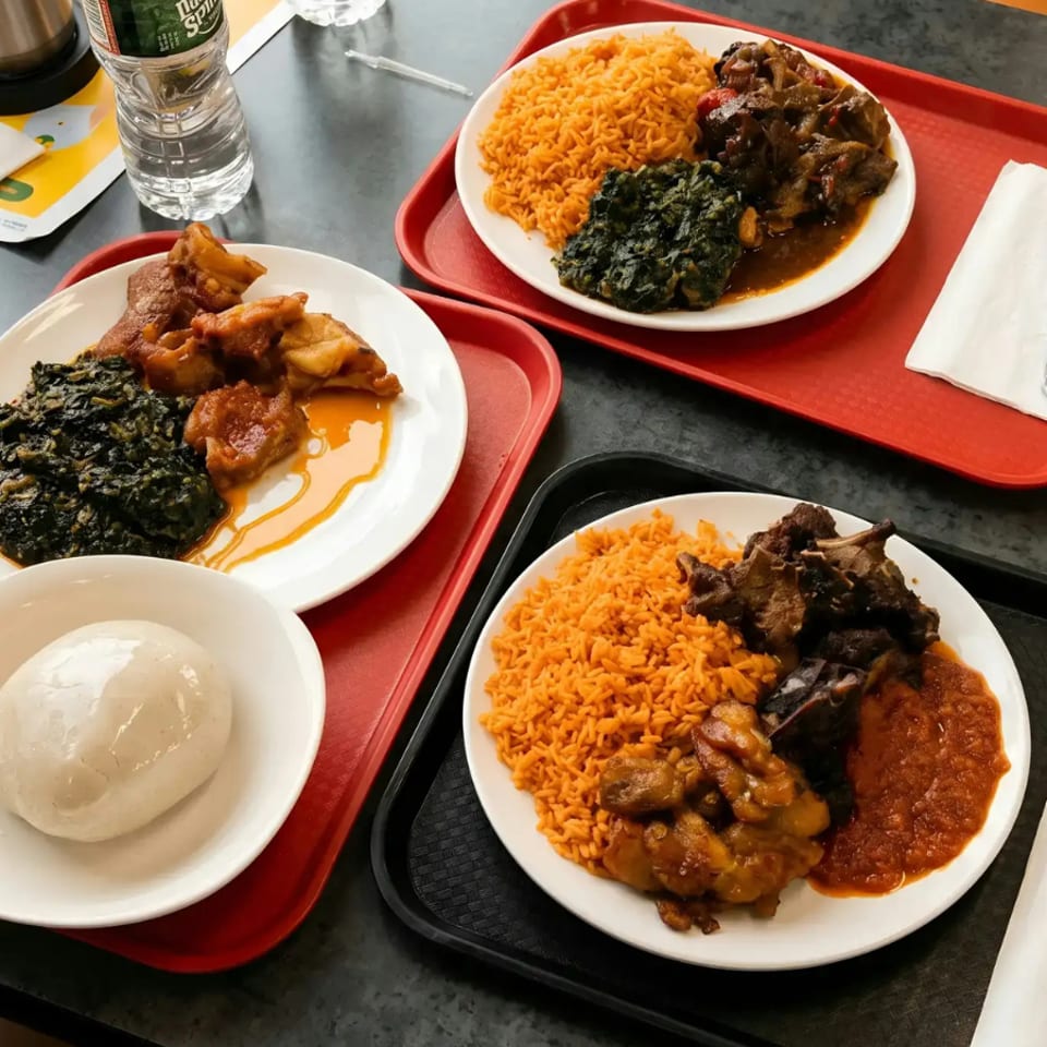 Three plates of jollof rice, stewed meat, and greens, with one plate also having fufu.